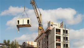 A crane lifts a prefabricated module into place on a construction site.