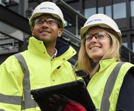 Two Balfour Beatty workers, one male, one female, wearing yellow hi-vis and white Balfour Beatty-branded hard hats.