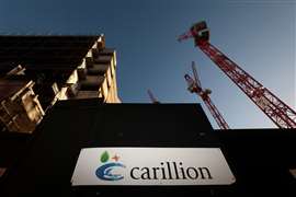 A sign bearing the Carillion logo on the hoarding of a UK construction site, with a tower crane in the background.