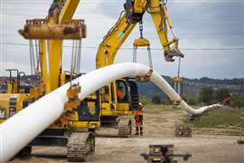 Construction machinery lifts a long white pipeline into place
