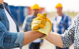 Close-up of two construction workers' gloved hands clasped together in a gesture of collaboration