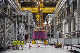 A group of people wearing yellow hi-vis vests and hard hats stand in a vast hall at the ITER project.