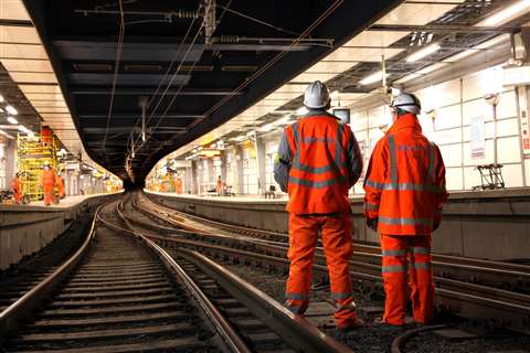 Two Balfour Beatty workers in branded orange hi-vis workwear and white hard hats stand on a railway track.